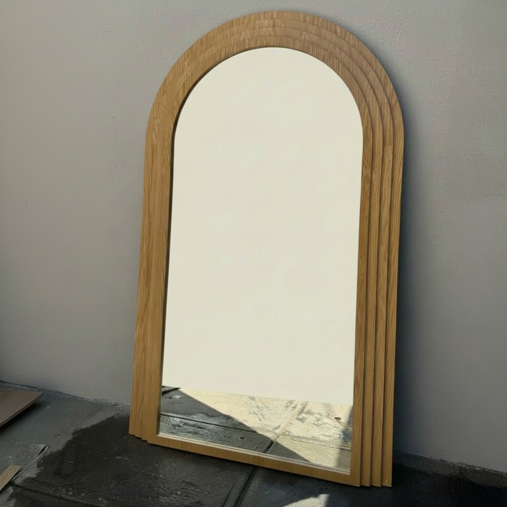 Espejo con marco de mader e forma curvo, con vista lateral viendo el acabado del marco.