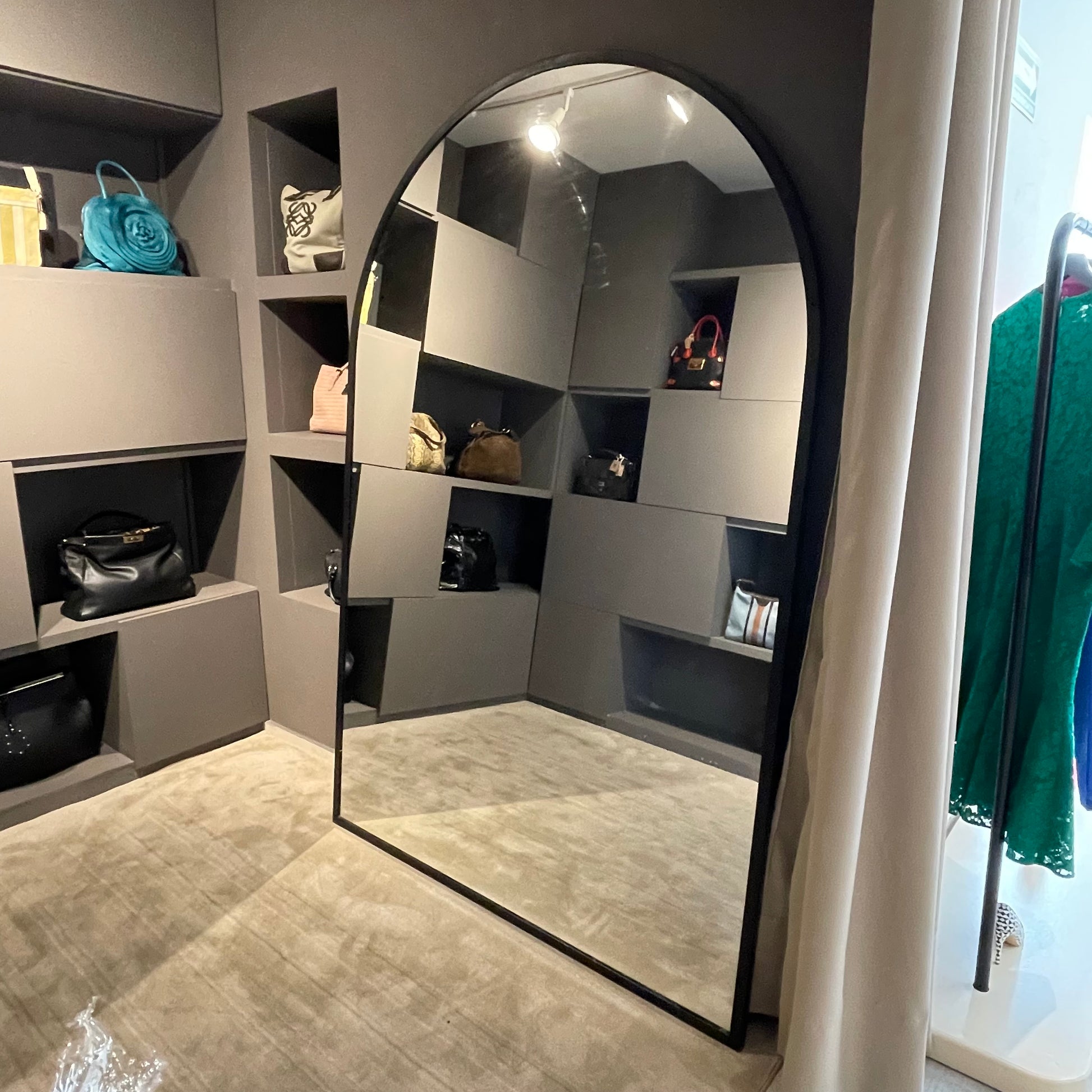 Espejo gigante con marco, con forma arqueada, colocada en una boutique.