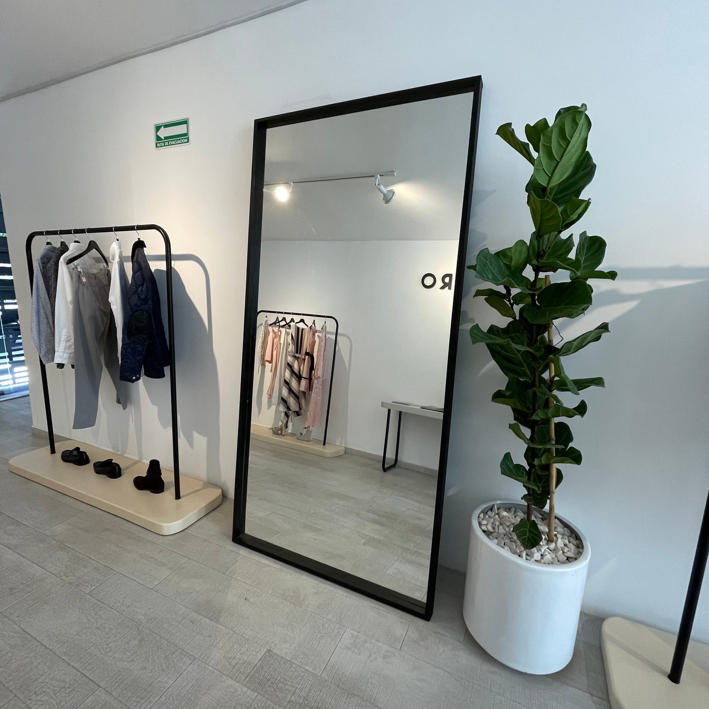 Espejo gigante, con marco color negro, luciendo dentro de una boutique.